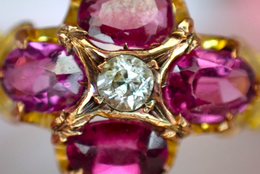 An antique Victorian 15ct yellow gold ring featuring four oval almandine garnets centred around a single old-cut diamond with carved scroll shoulders. View V