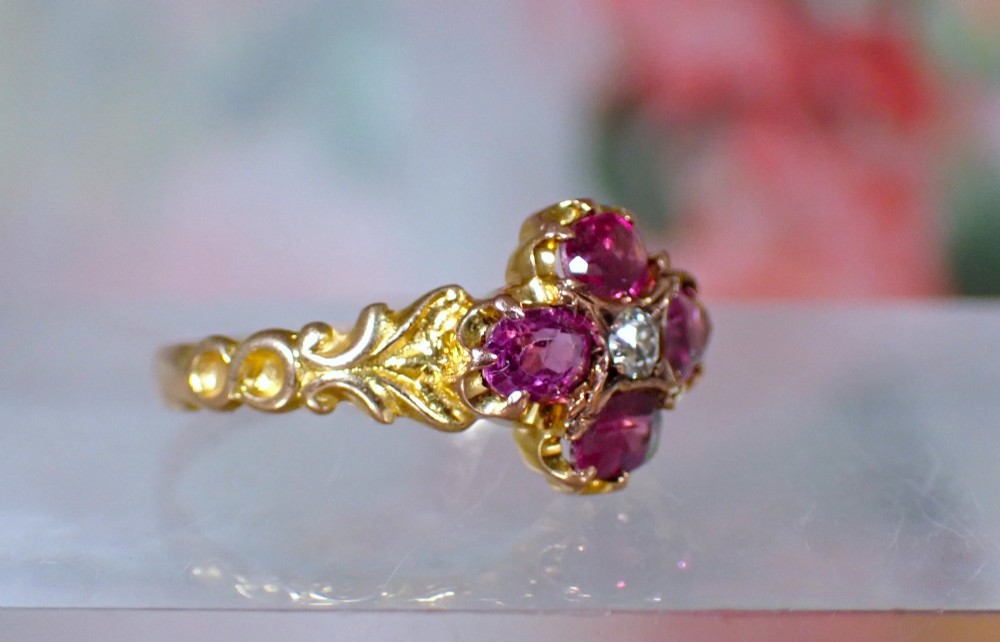 An antique Victorian 15ct yellow gold ring featuring four oval almandine garnets centred around a single old-cut diamond with carved scroll shoulders. View VI