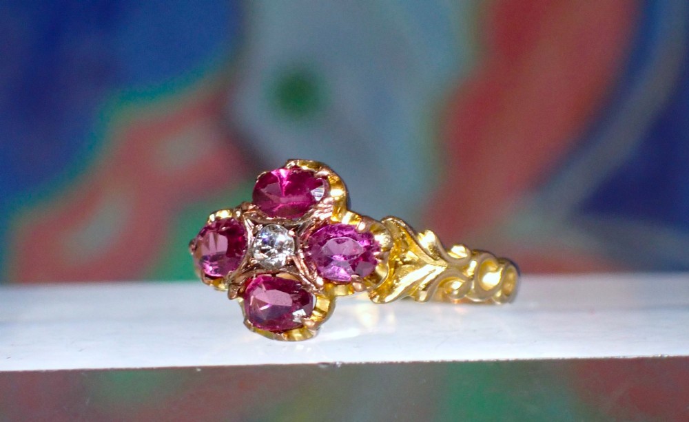 An antique Victorian 15ct yellow gold ring featuring four oval almandine garnets centred around a single old-cut diamond with carved scroll shoulders. View VII
