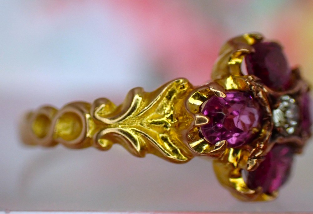 An antique Victorian 15ct yellow gold ring featuring four oval almandine garnets centred around a single old-cut diamond with carved scroll shoulders. View VIII