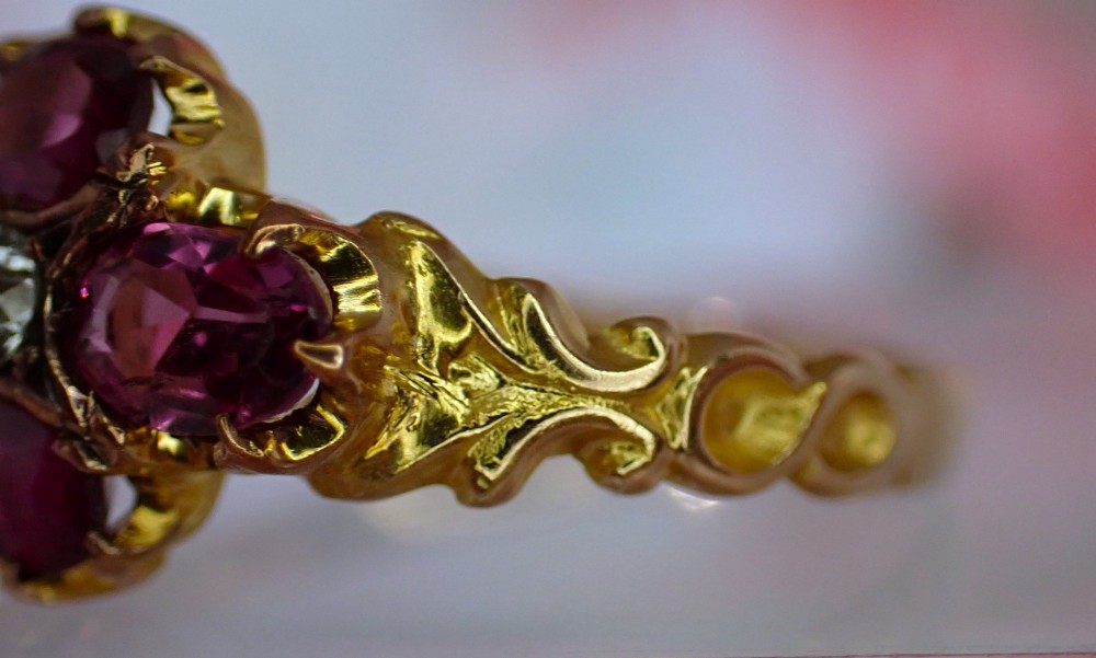 An antique Victorian 15ct yellow gold ring featuring four oval almandine garnets centred around a single old-cut diamond with carved scroll shoulders. View X