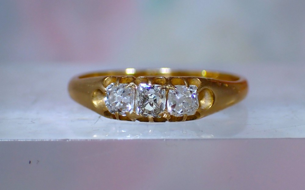 An 18ct yellow gold Victorian ring featuring three cushion cut diamonds set in a carved row along the band.
