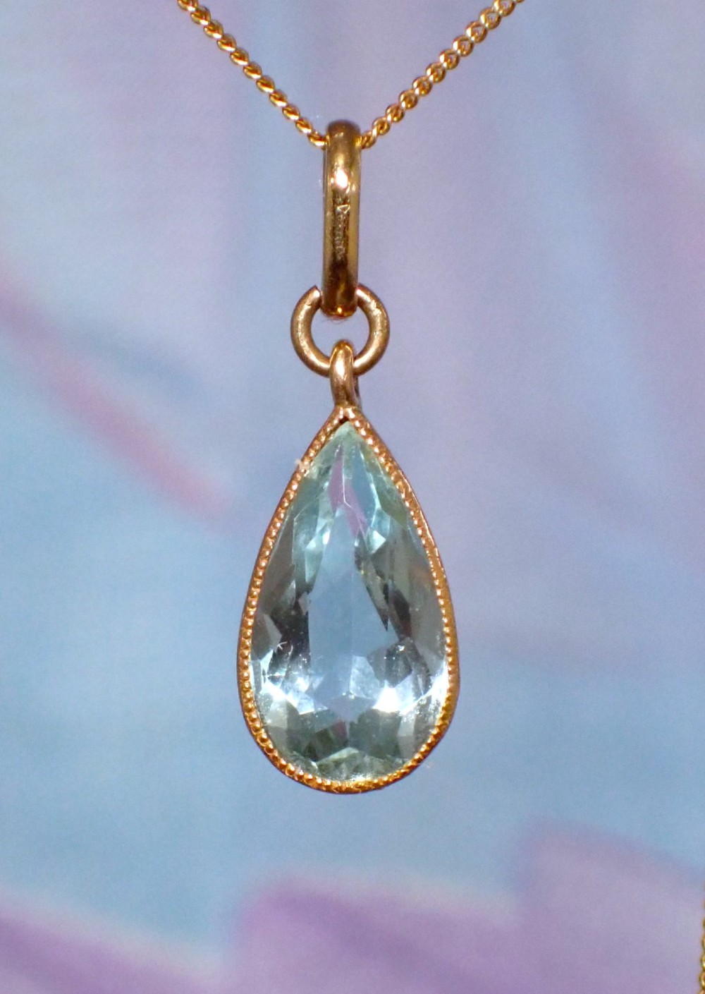 A pear-shaped pale blue aquamarine gemstone set in a yellow gold bezel pendant suspended from a fine gold chain. View II