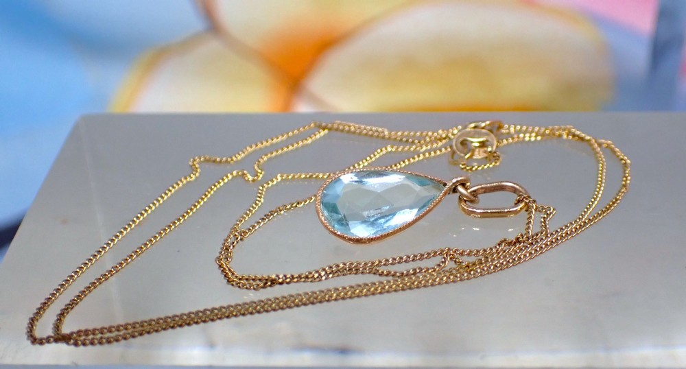 A pear-shaped pale blue aquamarine gemstone set in a yellow gold bezel pendant suspended from a fine gold chain. View V