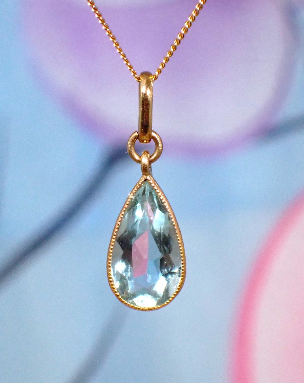 A pear-shaped pale blue aquamarine gemstone set in a yellow gold bezel pendant suspended from a fine gold chain. View VI