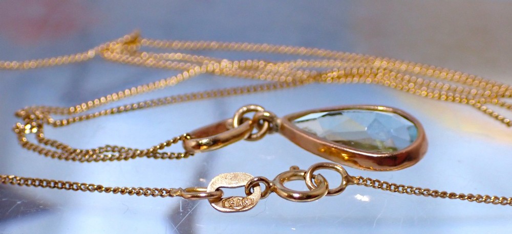 A pear-shaped pale blue aquamarine gemstone set in a yellow gold bezel pendant suspended from a fine gold chain. View VII