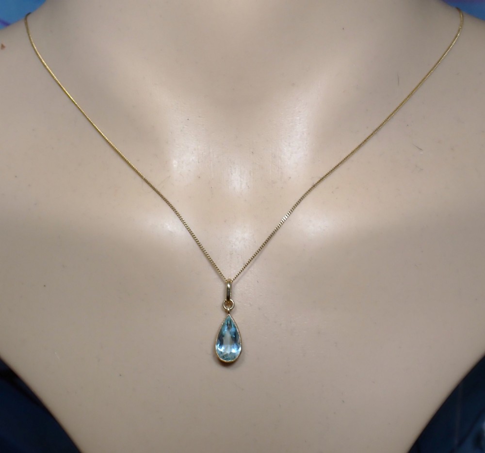 A pear-shaped pale blue aquamarine gemstone set in a yellow gold bezel pendant suspended from a fine gold chain. View VIII