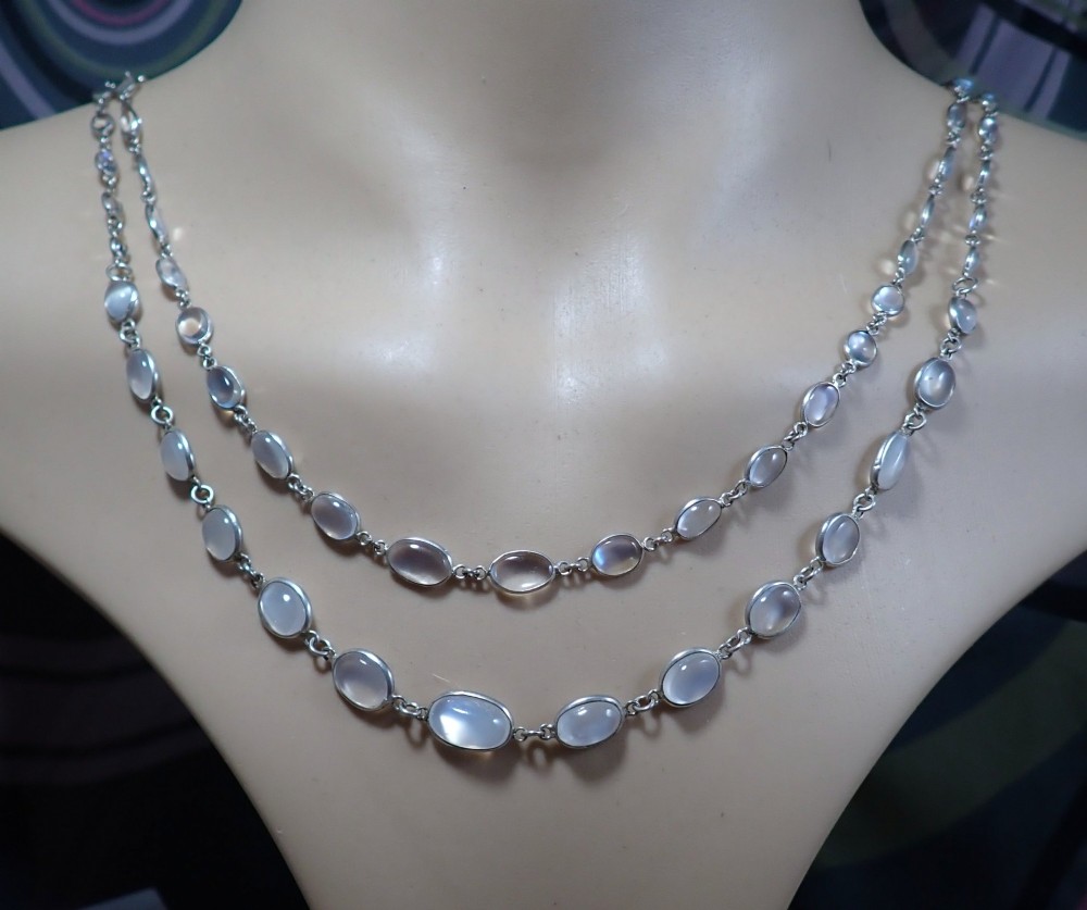 An antique Arts and Crafts sterling silver double-strand necklace featuring bezel-set oval cabochon moonstones linked together by wire chain loops.