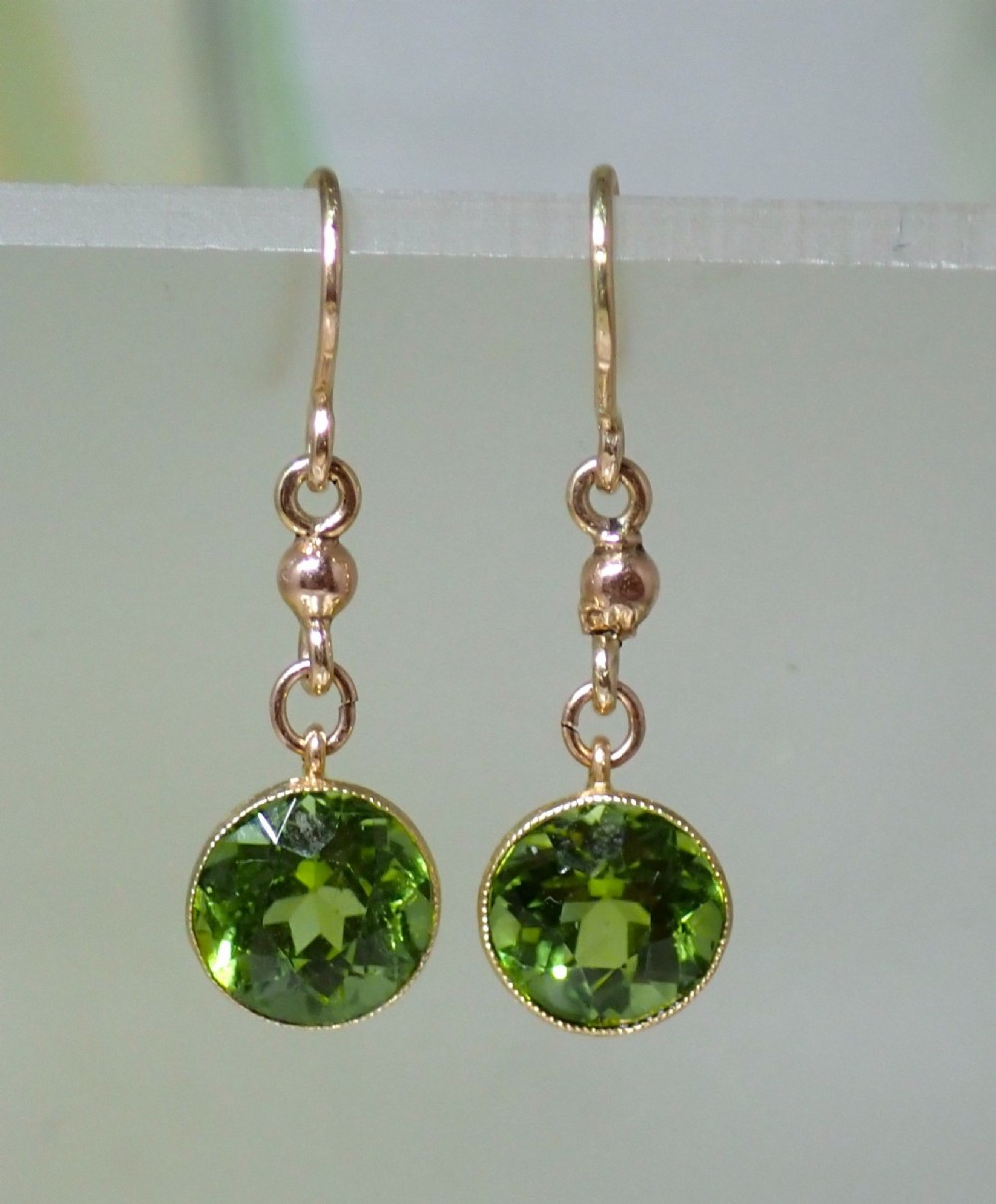 Pair of antique Edwardian 15ct gold drop earrings featuring circular faceted green peridots in collet settings suspended from wire hooks.
