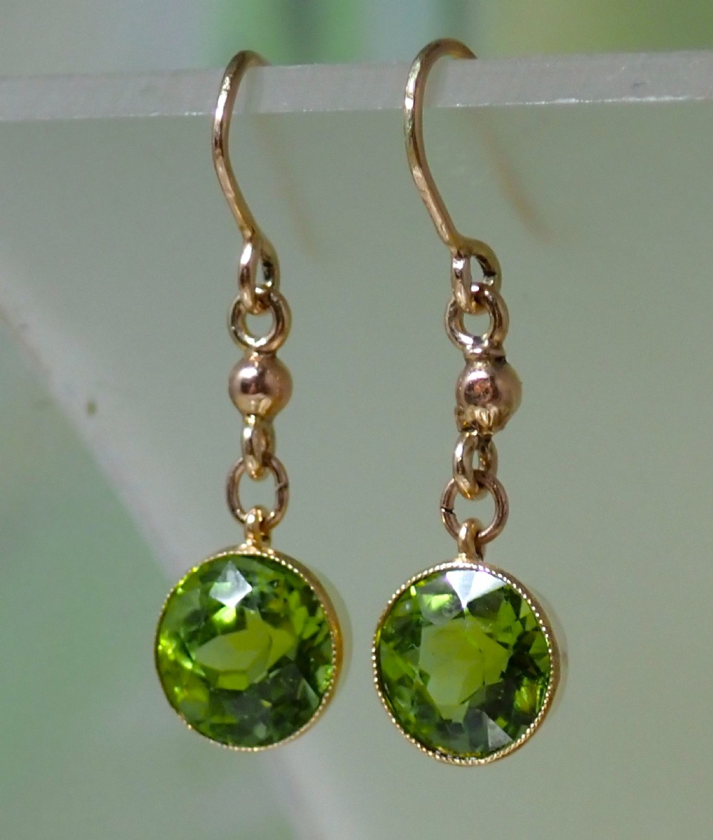 Pair of antique Edwardian 15ct gold drop earrings featuring circular faceted green peridots in collet settings suspended from wire hooks. View III