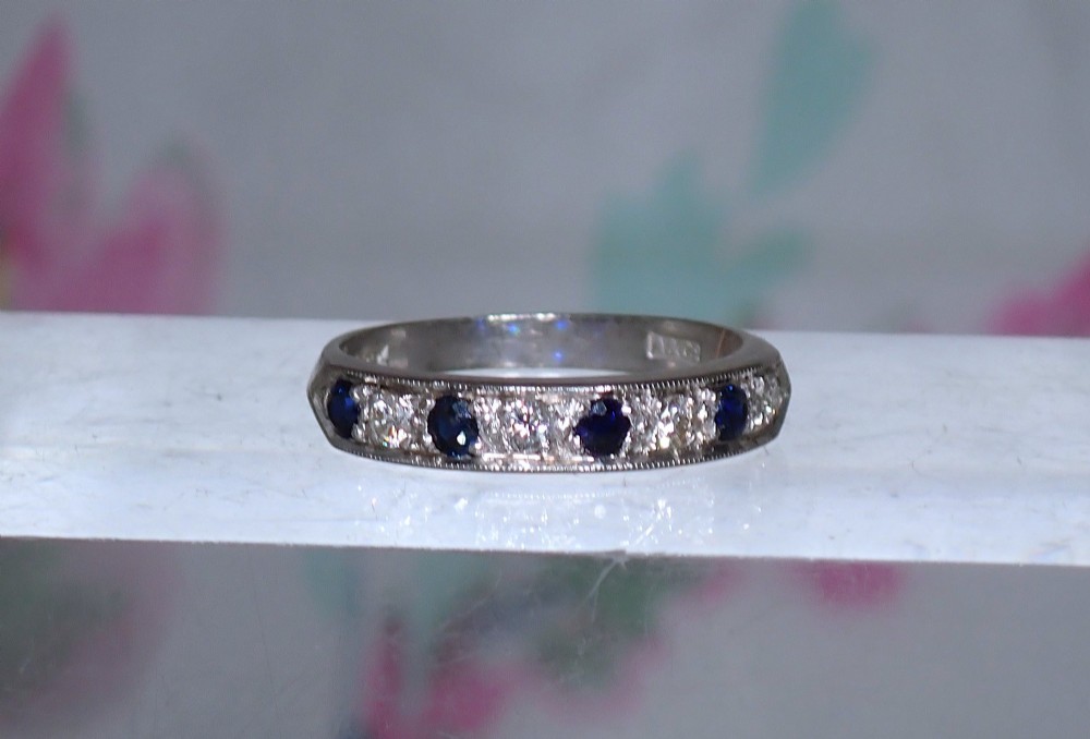 A vintage 18ct white gold half eternity ring featuring alternating round dark blue sapphires and clear diamonds along the band.
