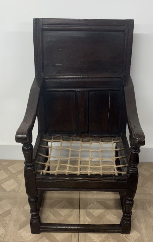 fig 1. A 17th-century dark oak wainscot armchair featuring a solid panelled back, turned front supports, sturdy stretchers, and a patterned fabric seat cushion.