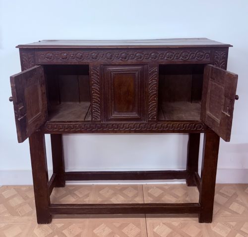 fig 2. A 17th-century joined dark oak cupboard on stand featuring carved guilloche friezes, panelled doors, and square stile legs joined by stretchers.