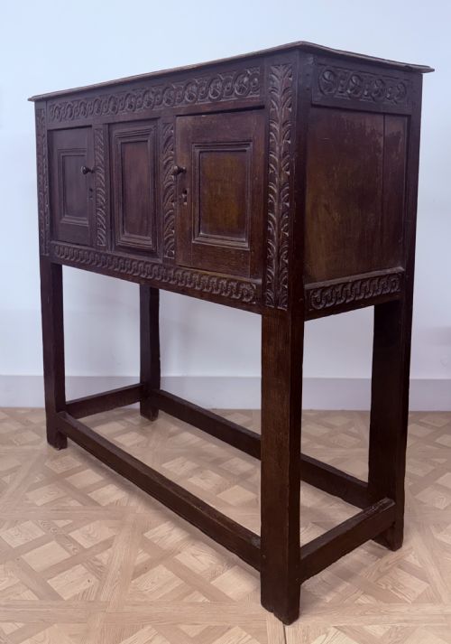 fig 3. A 17th-century joined dark oak cupboard on stand featuring carved guilloche friezes, panelled doors, and square stile legs joined by stretchers.