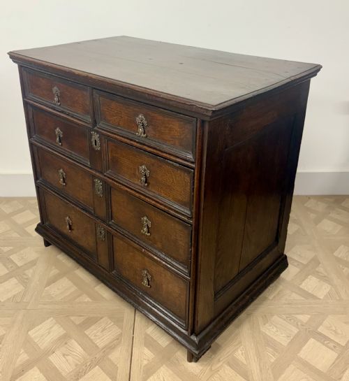 fig 2. A late 17th-century dark oak chest of drawers featuring geometric moulded panel drawer fronts and decorative brass drop handles.