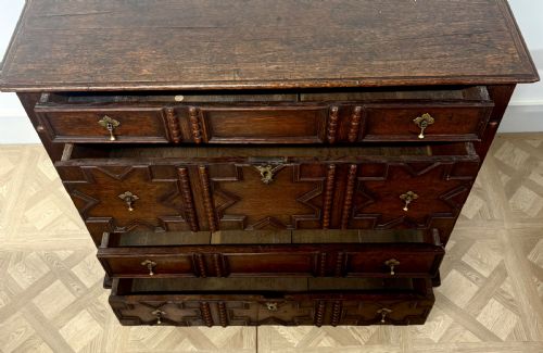 fig 1. A seventeenth-century dark oak chest of drawers featuring geometric applied mouldings, bobbin detailing, and brass drop handles.