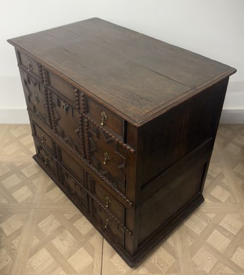 fig 2. A seventeenth-century dark oak chest of drawers featuring geometric applied mouldings, bobbin detailing, and brass drop handles.