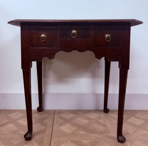 fig 1. An early 18th-century dark oak side table featuring three drawers with brass ring pulls, a scalloped apron, and slender cabriole legs ending in pad feet.