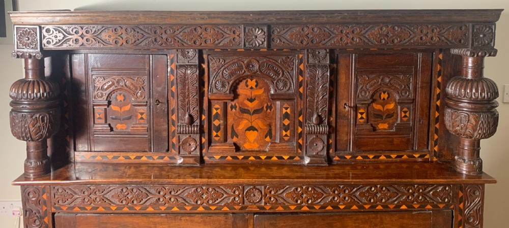 A 17th-century Elizabethan carved oak court cupboard featuring inlaid geometric panels, cup-and-cover supports, and arcaded lower doors. View VIII