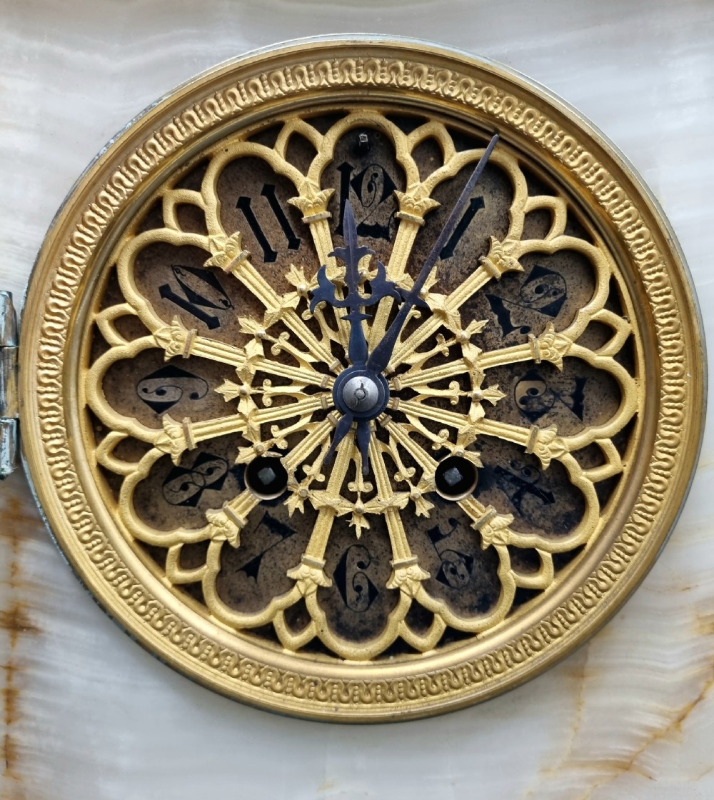 A nineteenth-century cream onyx mantel clock featuring gilt bronze mounts, classical columns, a decorative pierced dial, and a small bust of William Shakespeare mounted at the top. View V