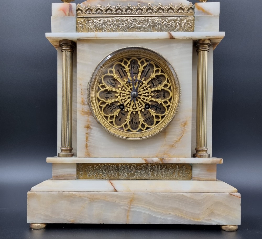 A nineteenth-century cream onyx mantel clock featuring gilt bronze mounts, classical columns, a decorative pierced dial, and a small bust of William Shakespeare mounted at the top. View XIII