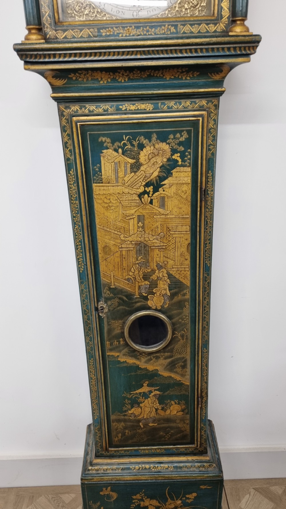 An 18th-century green and gold Japanned longcase clock featuring hand-painted Chinoiserie landscapes, an arched brass dial, and gilt finials. View IX