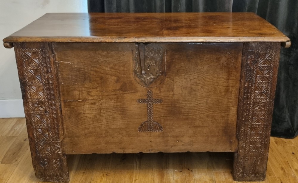 A dark stained oak coffer with carved geometric border panels, a central carved cross design, and a wrought iron escutcheon on the front.