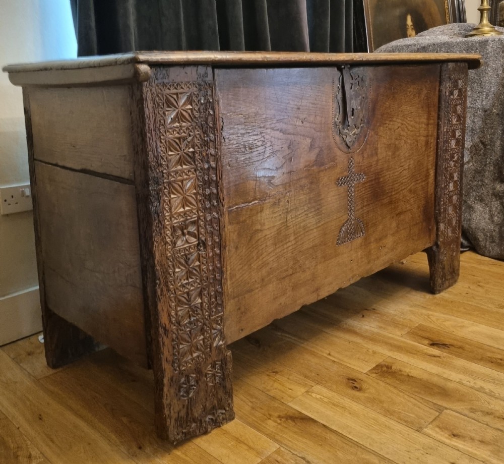 A dark stained oak coffer with carved geometric border panels, a central carved cross design, and a wrought iron escutcheon on the front. View III