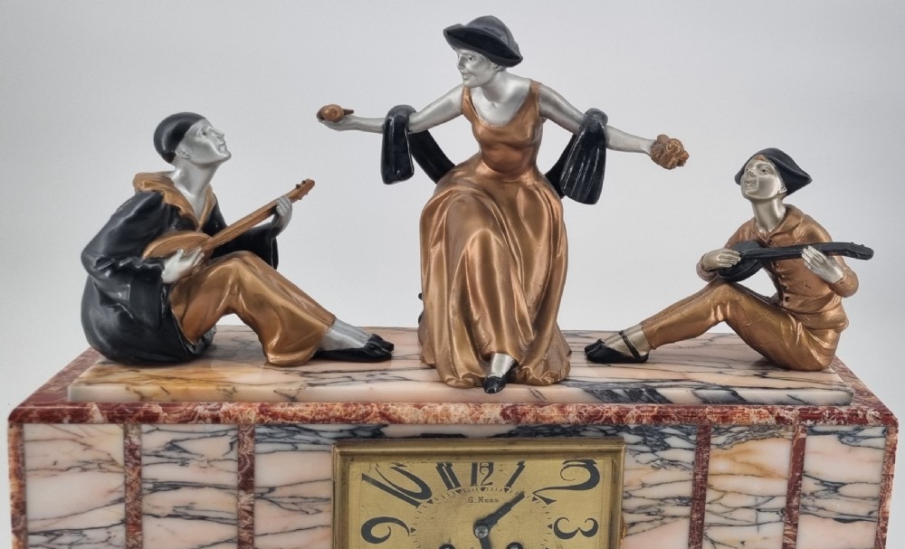An Art Deco mantel clock featuring a veined marble base with a rectangular brass dial, surmounted by three patinated metallic figures depicting musicians and a dancer. View III