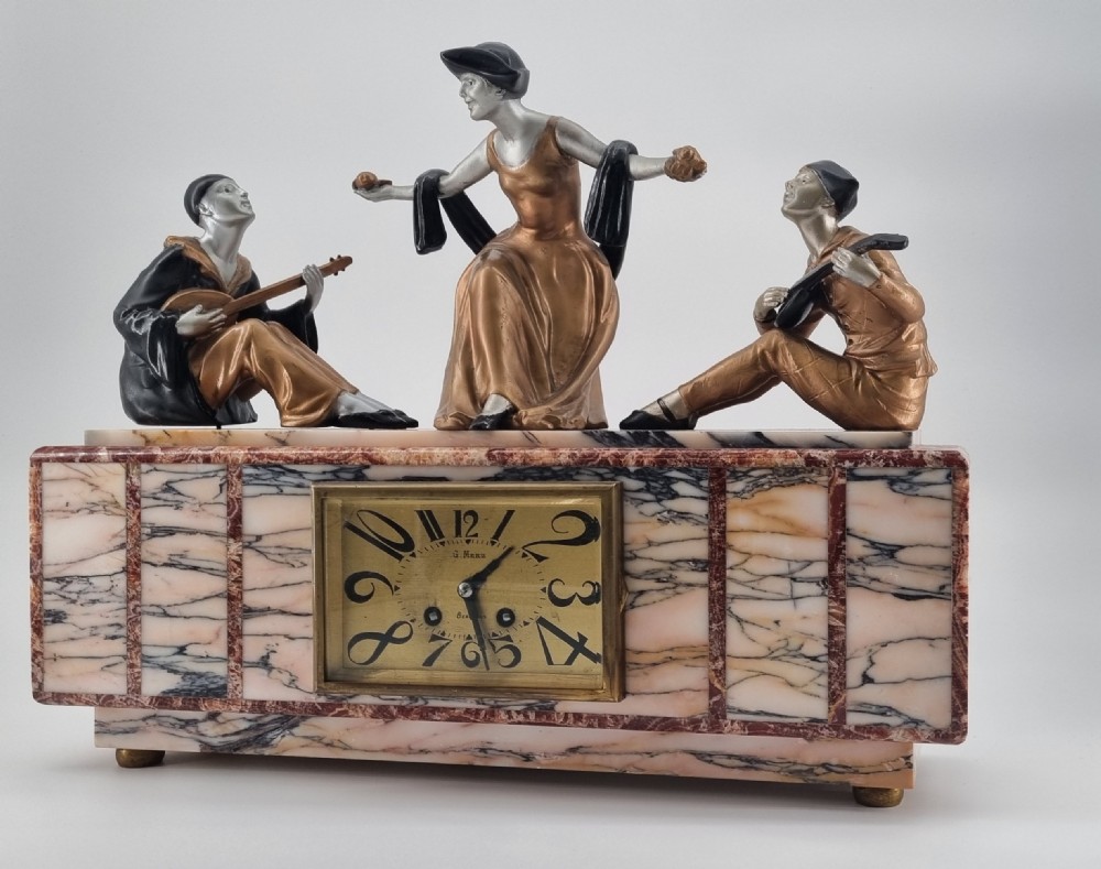 An Art Deco mantel clock featuring a veined marble base with a rectangular brass dial, surmounted by three patinated metallic figures depicting musicians and a dancer. View V
