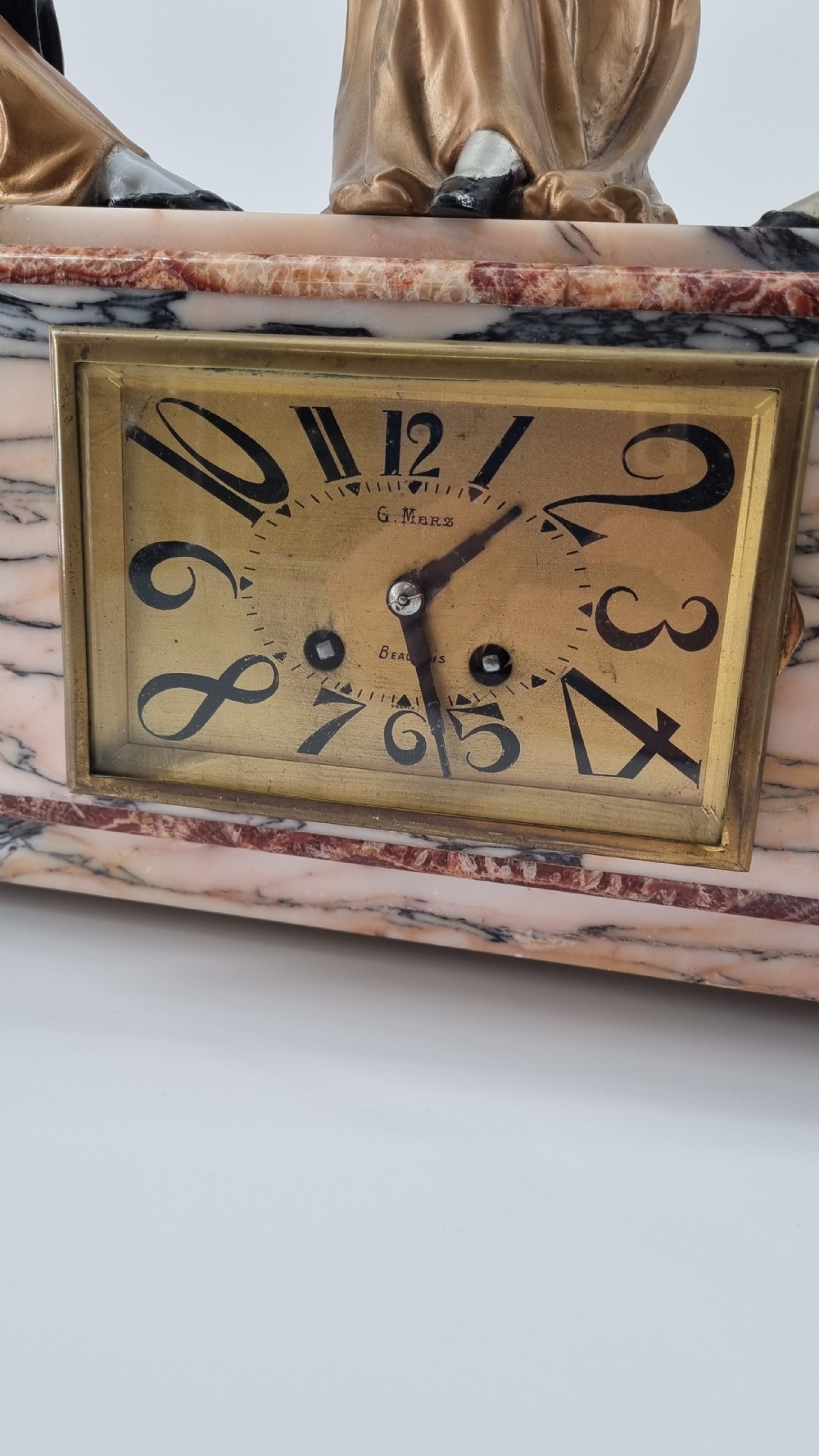 An Art Deco mantel clock featuring a veined marble base with a rectangular brass dial, surmounted by three patinated metallic figures depicting musicians and a dancer. View VII