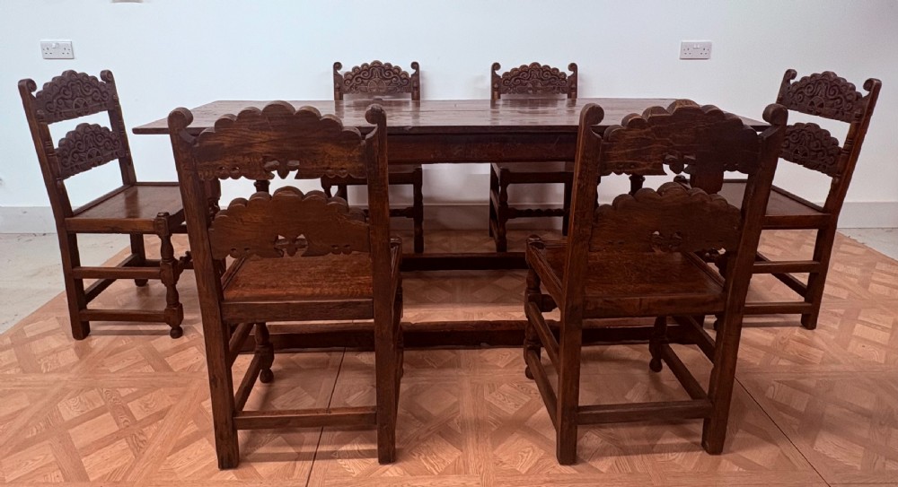 A dark oak refectory dining table paired with six matching carved wooden dining chairs set on a parquet floor.