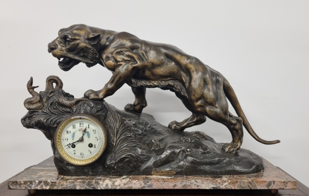 A dark patinated bronze sculpture of a tiger fighting a serpent set upon a rock housing a round clock dial, all resting on a rectangular veined marble base. View II