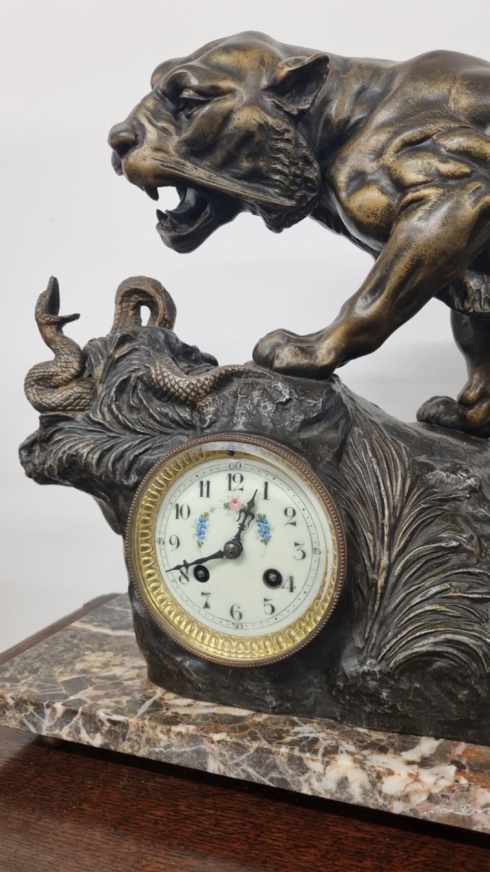 A dark patinated bronze sculpture of a tiger fighting a serpent set upon a rock housing a round clock dial, all resting on a rectangular veined marble base. View V