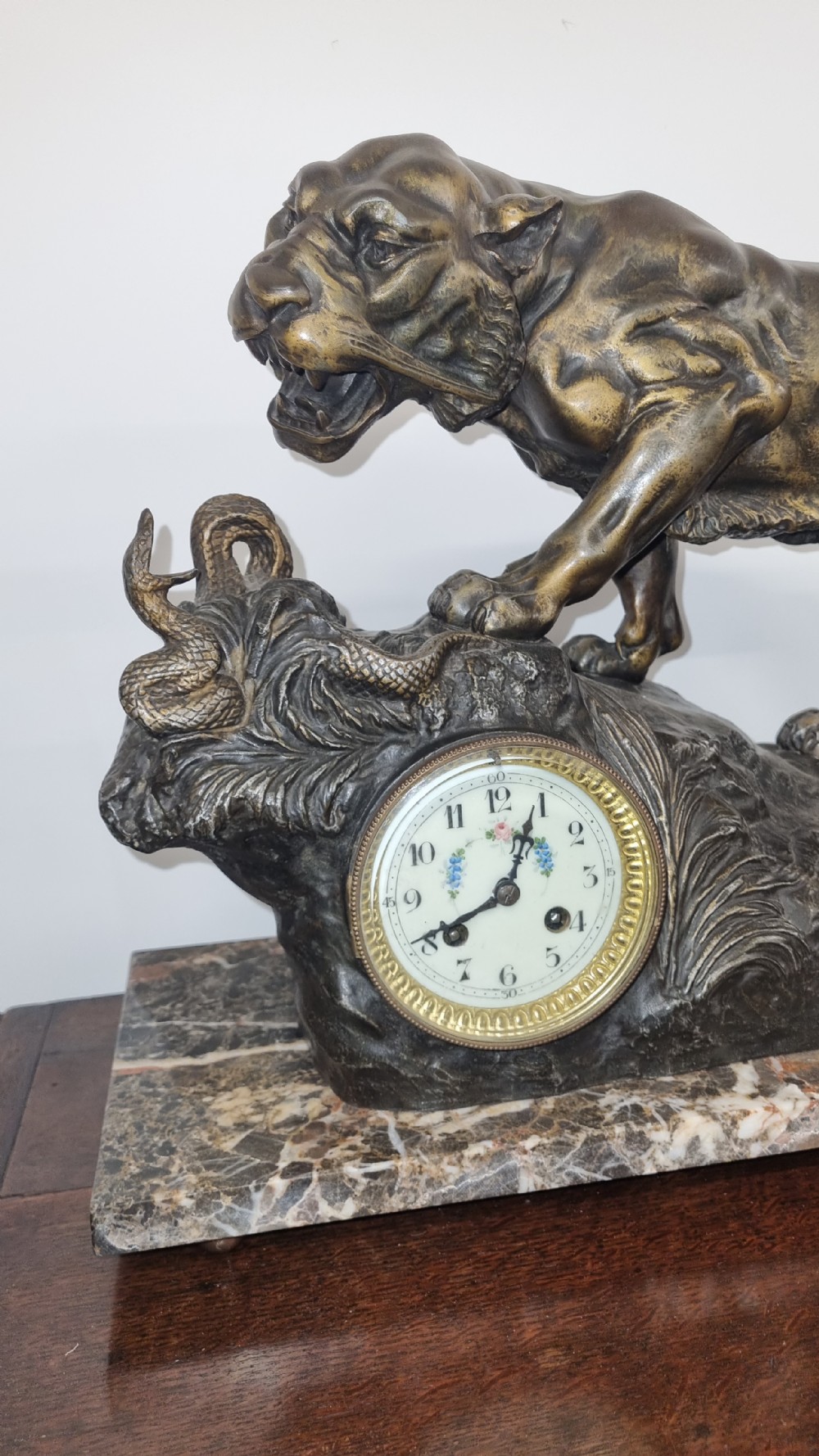 A dark patinated bronze sculpture of a tiger fighting a serpent set upon a rock housing a round clock dial, all resting on a rectangular veined marble base. View VI