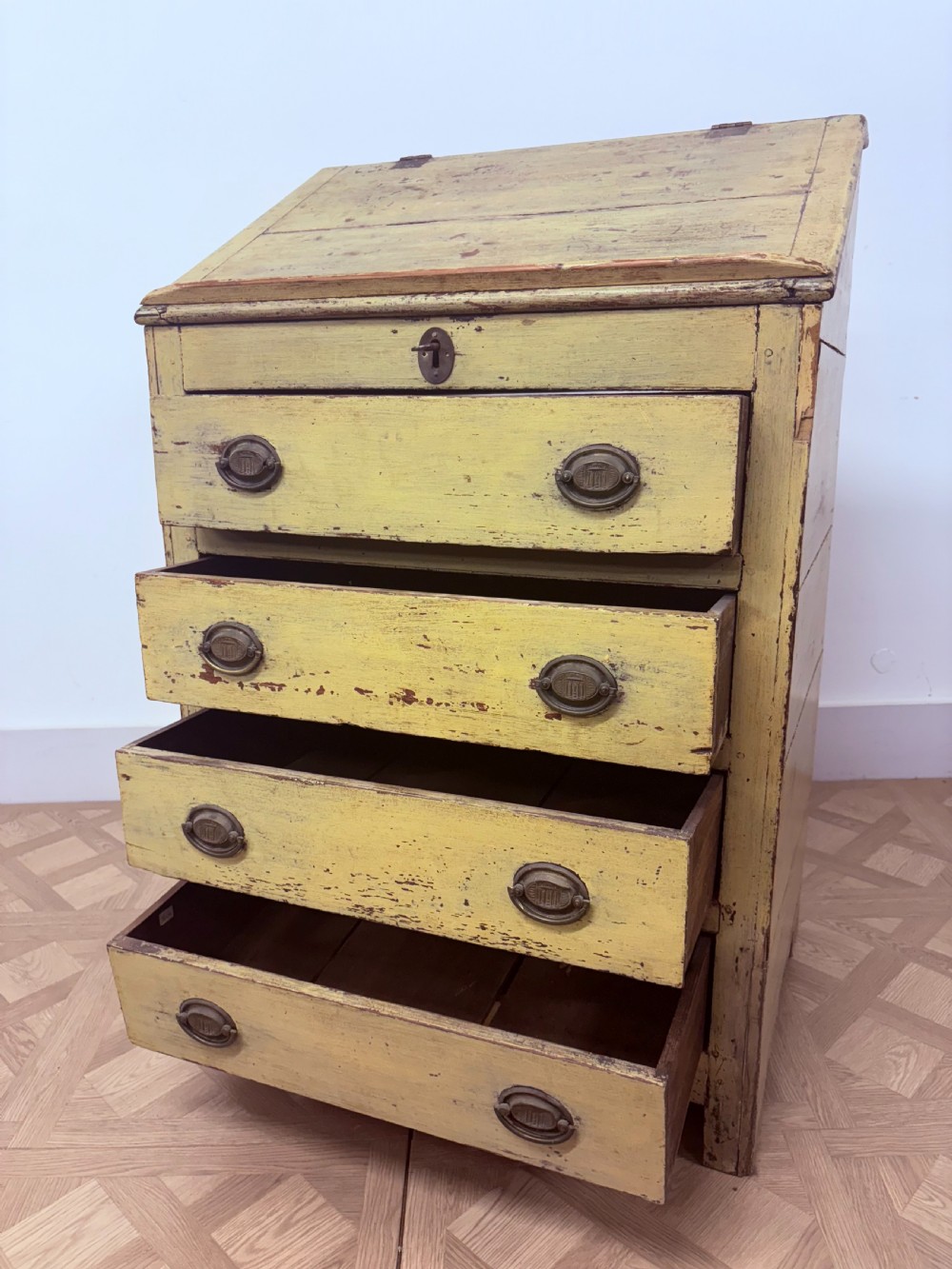 A late 18th-century English provincial chest of four drawers with a distressed yellow painted finish, brass handles, and an angled writing slope top. View V