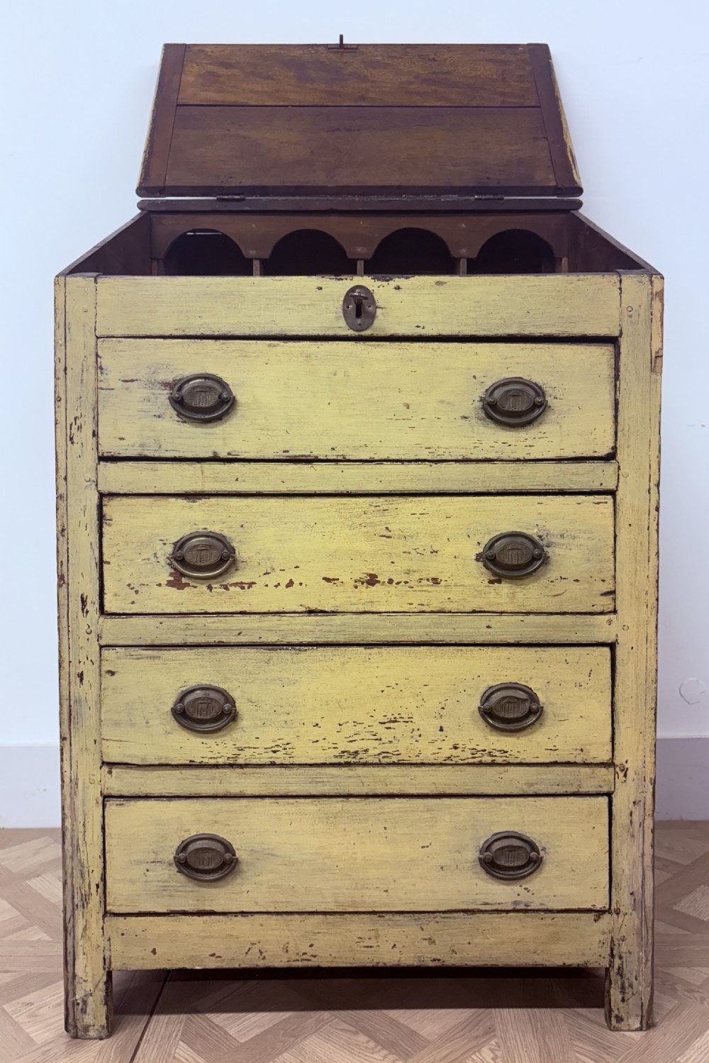 A late 18th-century English provincial chest of four drawers with a distressed yellow painted finish, brass handles, and an angled writing slope top. View VI