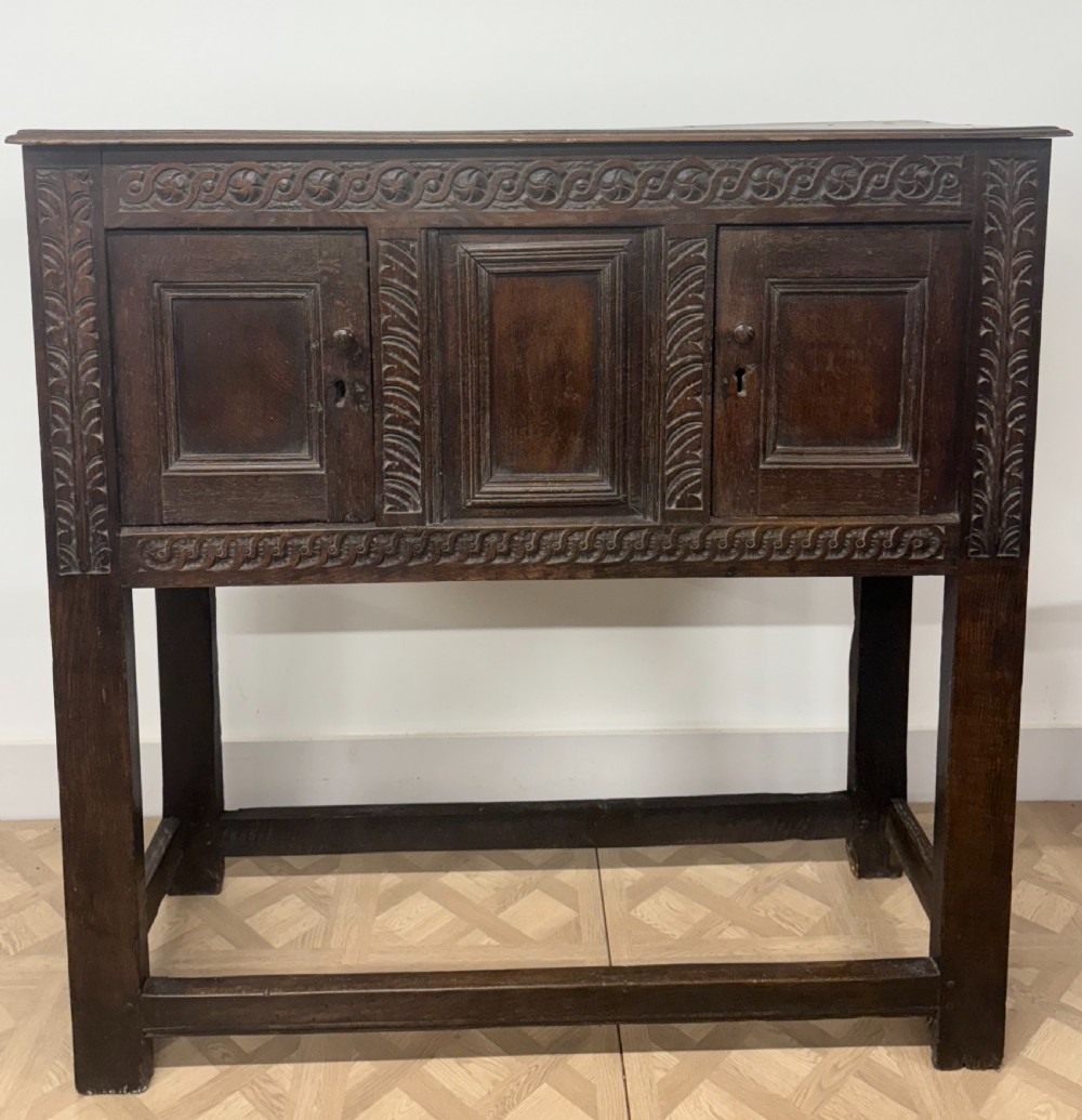 A 17th-century joined dark oak cupboard on stand featuring carved guilloche friezes, panelled doors, and square stile legs joined by stretchers. View VII