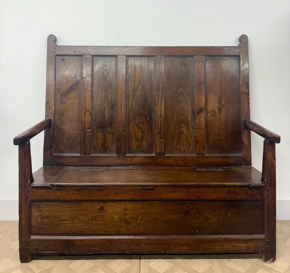 An 18th-century oak and ash box settle featuring a high five-panel back, straight armrests, and a hinged bench seat over a solid storage base. View II