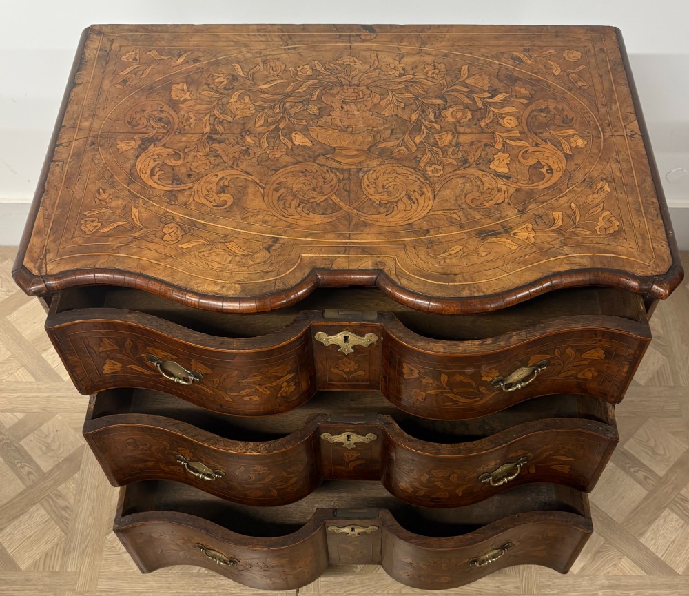 An eighteenth-century Dutch walnut chest of drawers featuring shaped drawer fronts with detailed floral marquetry inlays and decorative brass escutcheons. View VII