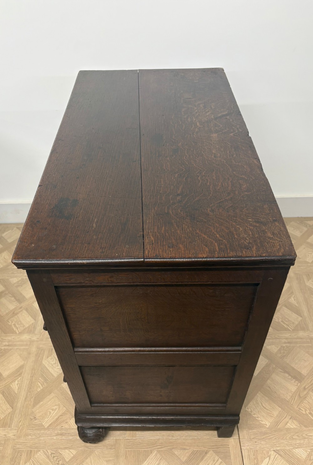 A late seventeenth-century dark oak chest of drawers featuring three geometrically panelled drawer fronts, brass teardrop handles, central escutcheons, and turned bun feet. View IV