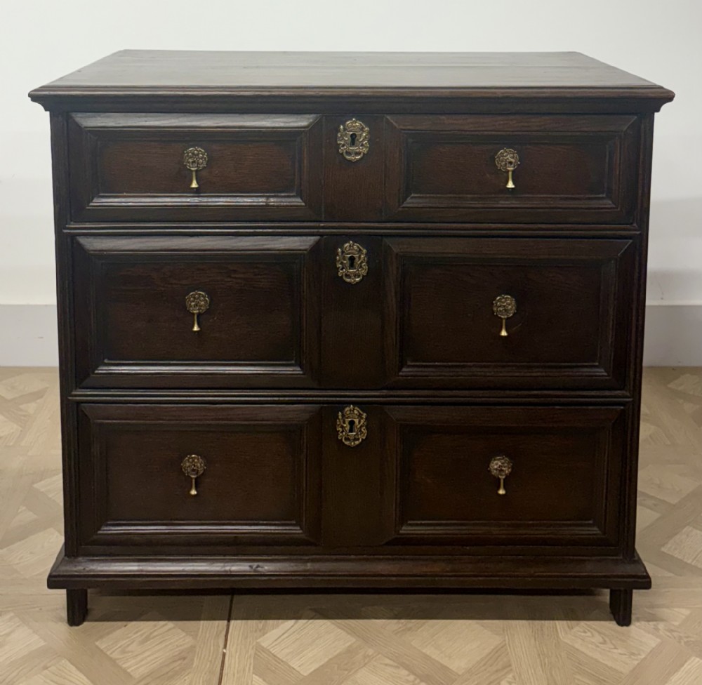 A seventeenth-century Charles II dark oak chest of drawers featuring three drawers with geometric moulded fronts and brass teardrop handles.