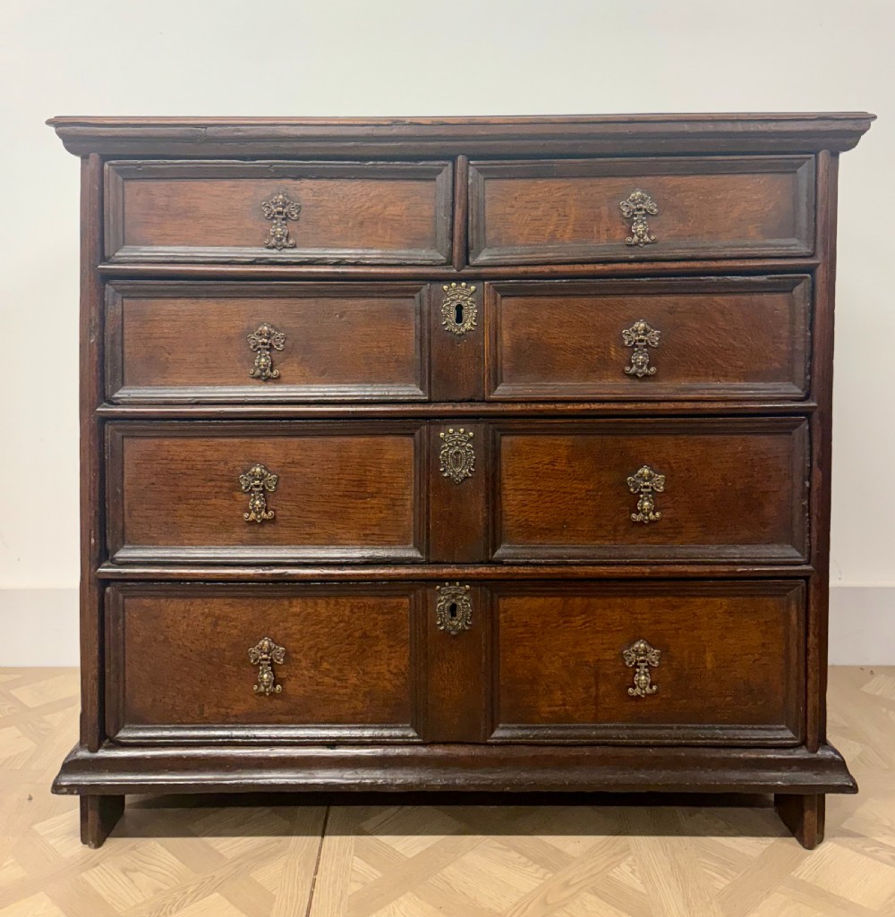 A late 17th-century dark oak chest of drawers featuring geometric moulded panel drawer fronts and decorative brass drop handles.