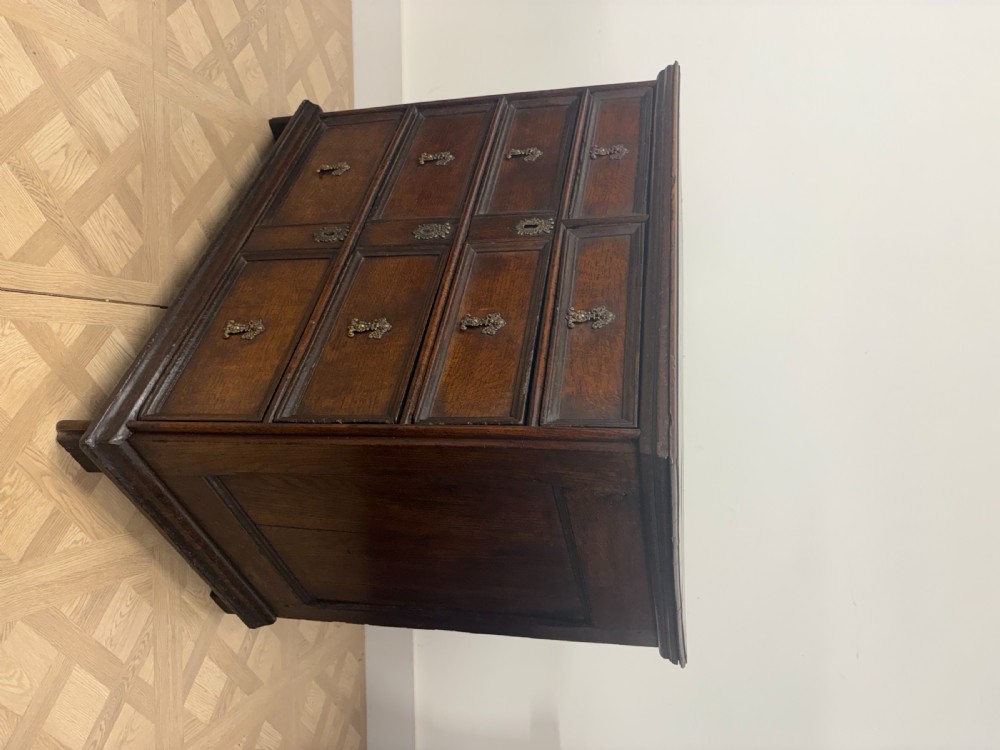 A late 17th-century dark oak chest of drawers featuring geometric moulded panel drawer fronts and decorative brass drop handles. View II