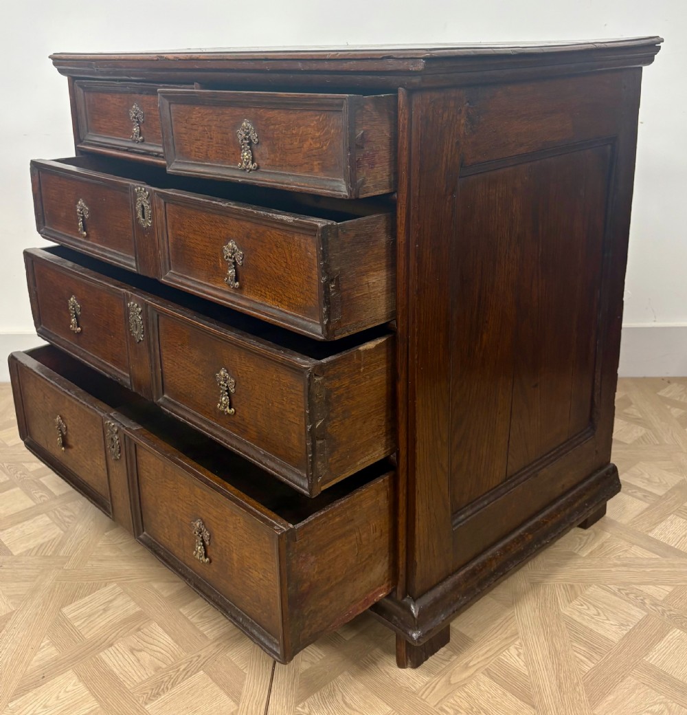A late 17th-century dark oak chest of drawers featuring geometric moulded panel drawer fronts and decorative brass drop handles. View IV