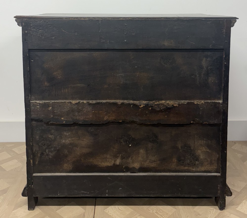 A late 17th-century dark oak chest of drawers featuring geometric moulded panel drawer fronts and decorative brass drop handles. View V
