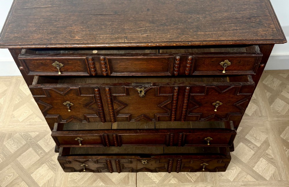 A seventeenth-century dark oak chest of drawers featuring geometric applied mouldings, bobbin detailing, and brass drop handles. View II