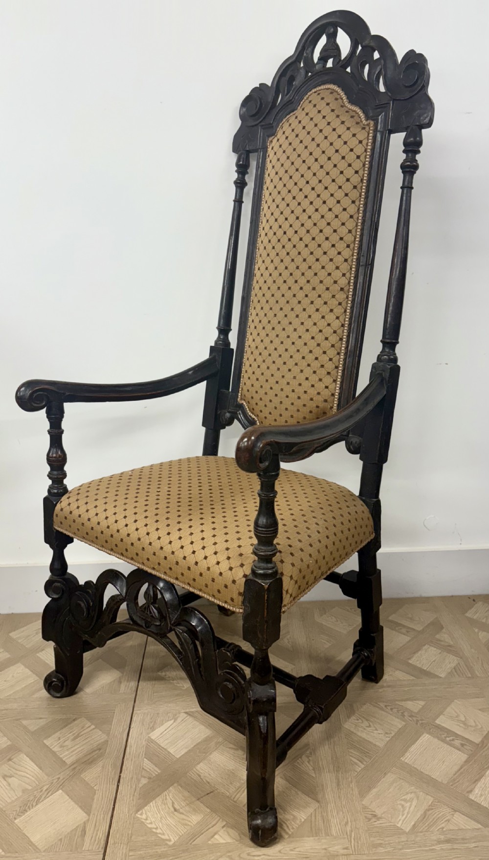 A late 17th-century Carolean carved dark walnut armchair featuring a tall padded backrest, scrolling arms, gold patterned upholstery, and an ornate carved stretcher.