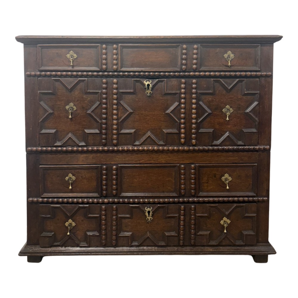 A seventeenth-century dark oak chest of drawers featuring geometric applied mouldings, bobbin detailing, and brass drop handles.
