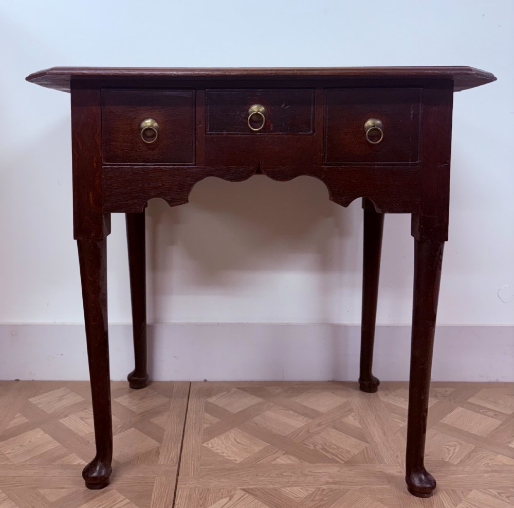 An early 18th-century dark oak side table featuring three drawers with brass ring pulls, a scalloped apron, and slender cabriole legs ending in pad feet. View II